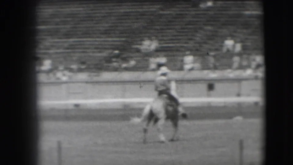 In 1941 Denver footage, a cowboy-hatted rider on horseback crosses a dirt arena before a distant crowd.