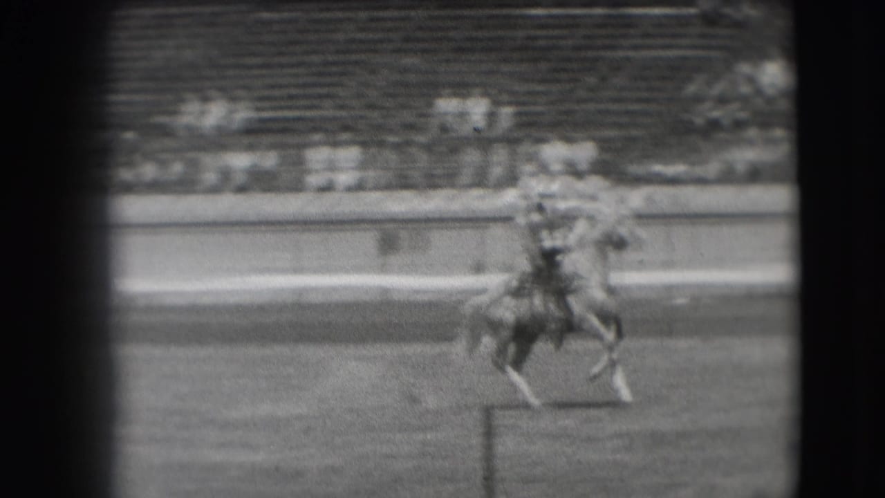 The rider continues across the Denver arena as the horse trots near the rail, with the crowd blurred behind.
