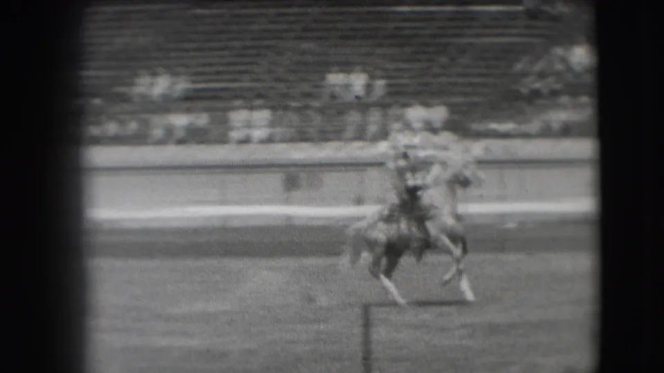 The rider continues across the Denver arena as the horse trots near the rail, with the crowd blurred behind.