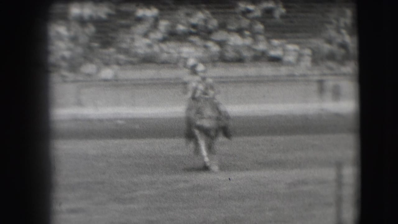 The rider and horse move toward the camera in the Denver arena, softened by black-and-white 8mm grain.