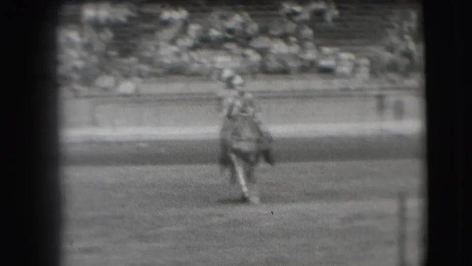 The rider and horse move toward the camera in the Denver arena, softened by black-and-white 8mm grain.