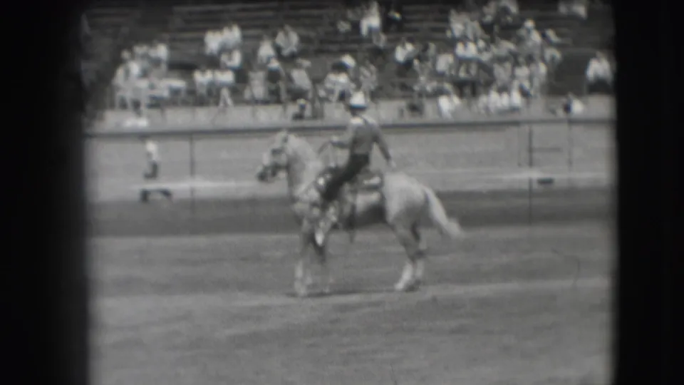 1941 Denver home-movie frame of a mounted rider on a light-colored horse with spectators seated in bleachers behind.