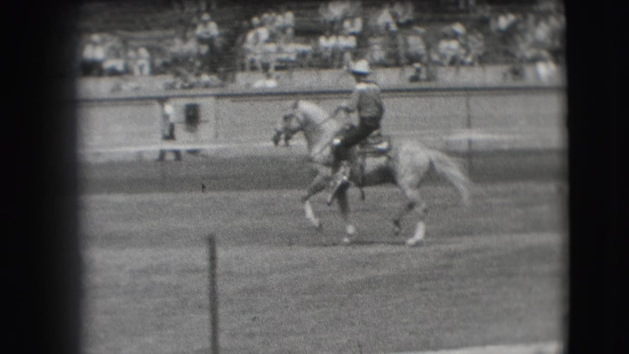 Mounted rider in a hat continues across a Denver equestrian arena in 1941, with bleachers visible behind the barrier.