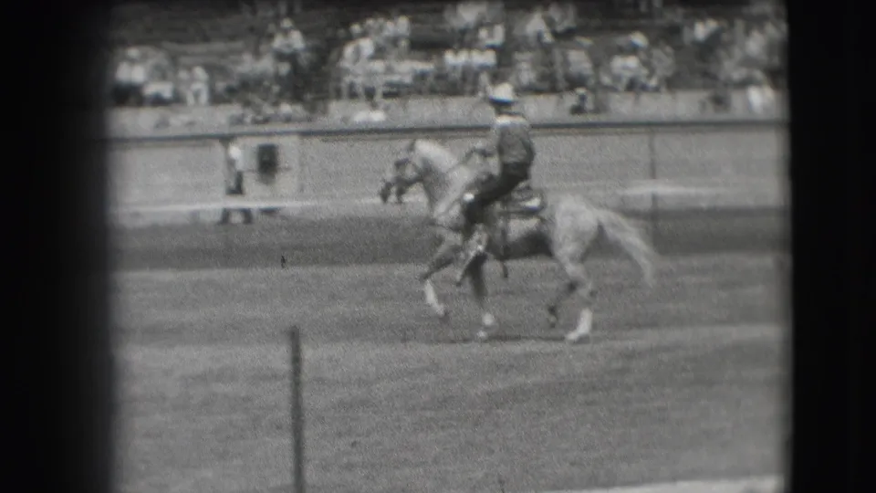 Mounted rider in a hat continues across a Denver equestrian arena in 1941, with bleachers visible behind the barrier.