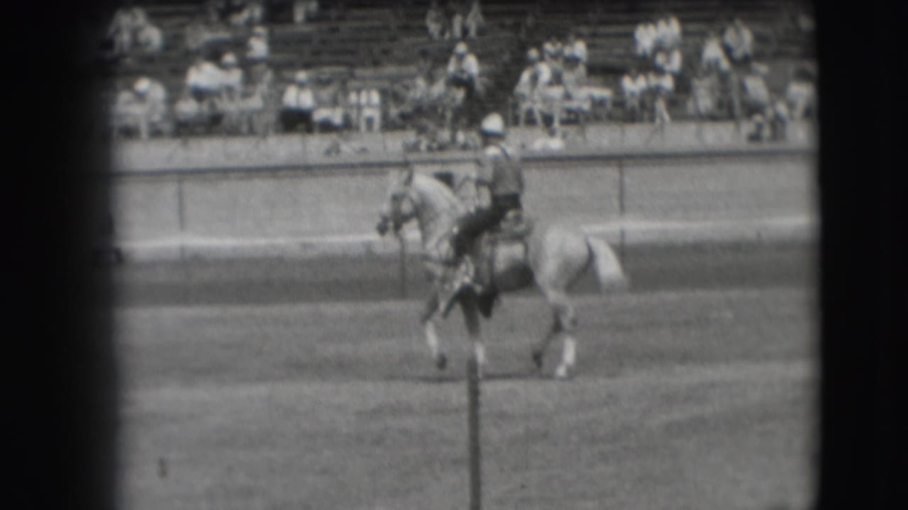 1941 Denver frame showing the rider and light-colored horse moving across the arena, partly crossed by a foreground post.