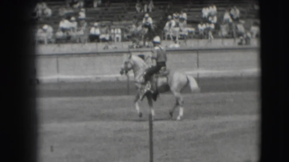 1941 Denver frame showing the rider and light-colored horse moving across the arena, partly crossed by a foreground post.