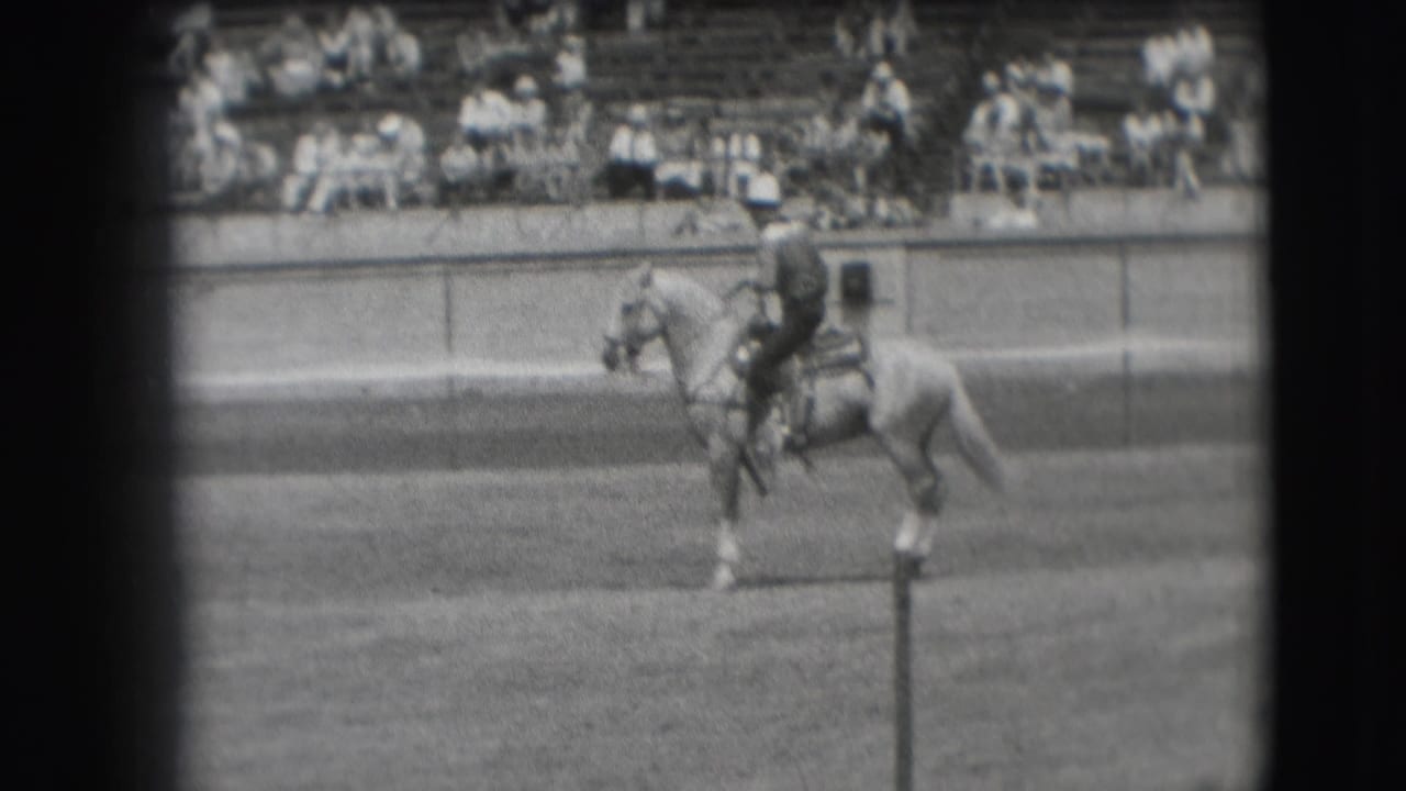Rider and horse continue across the arena in front of distant bleachers.