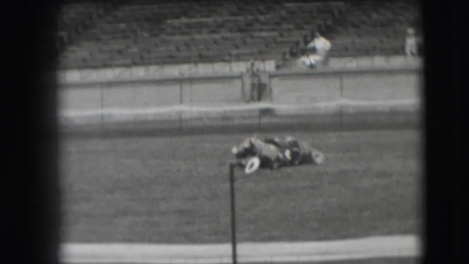 The horse lies on the grassy arena field beside a pole in the 1941 Denver home-movie footage, with mostly empty stadium seats behind.