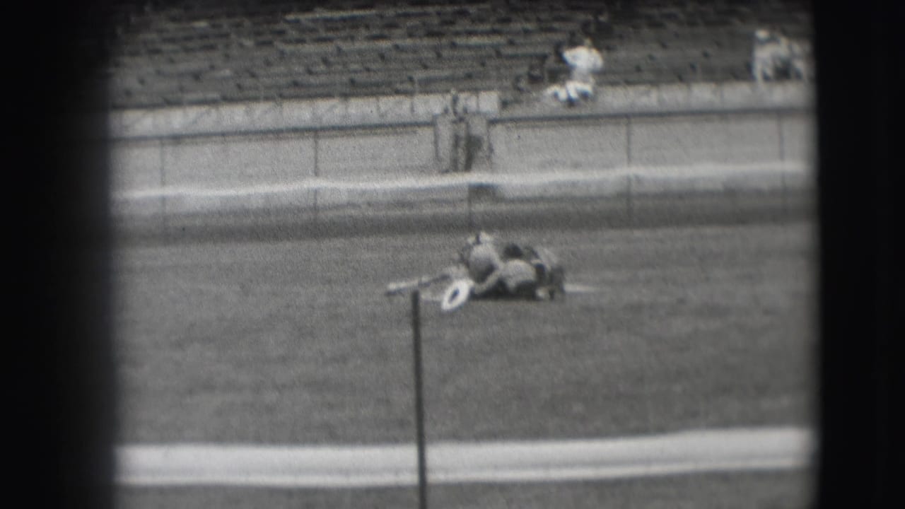 1941 Denver 8mm frame showing a cowboy and horse lying together in a grassy arena, viewed from a distant spectator angle.