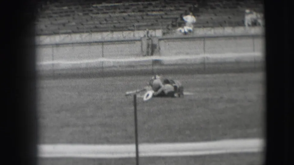 1941 Denver 8mm frame showing a cowboy and horse lying together in a grassy arena, viewed from a distant spectator angle.