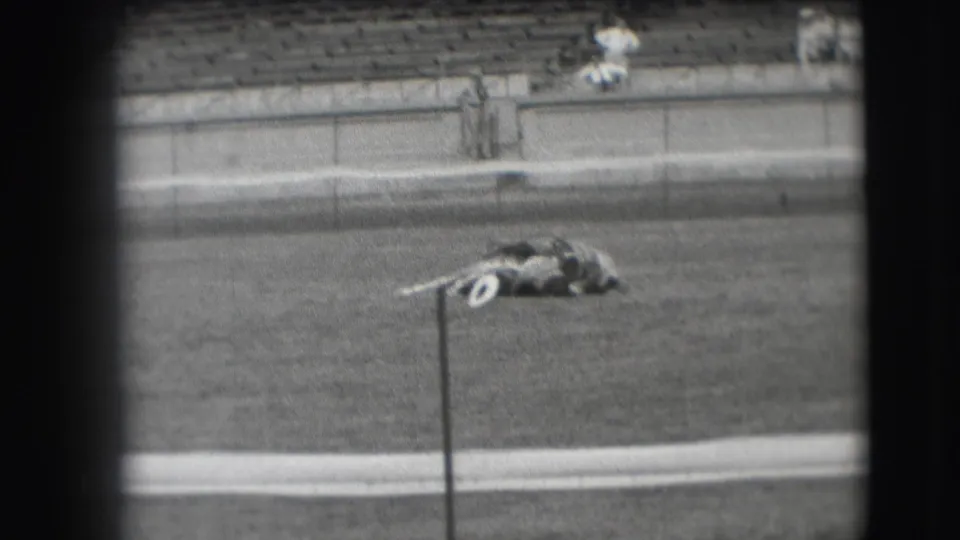 1941 Denver home-movie frame with a cowboy and horse still lying low in an arena, backed by mostly empty bleachers.