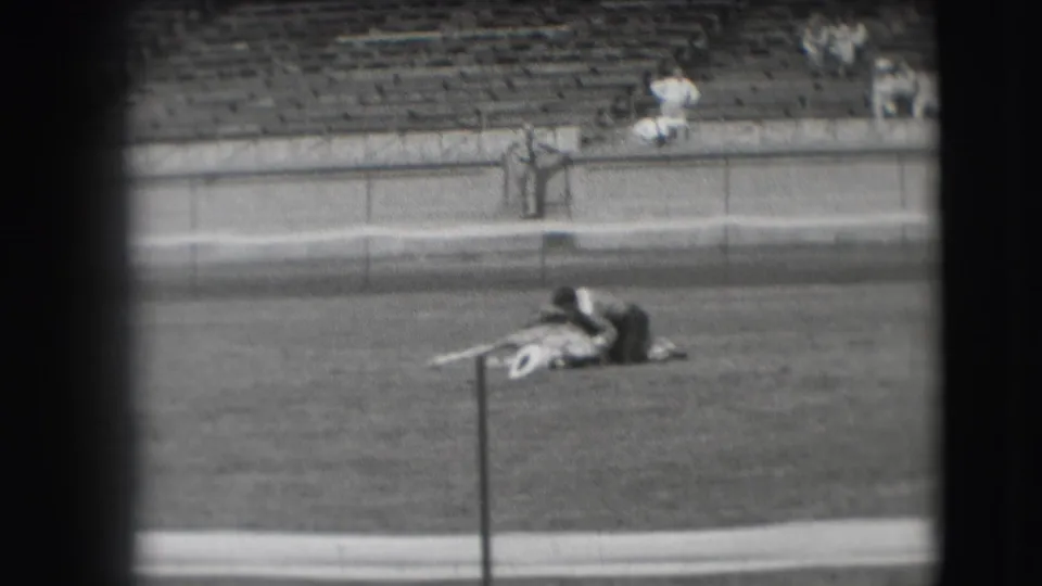 In 1941 Denver home-movie footage, a man lies across a bridled horse on a grass field near stadium bleachers.