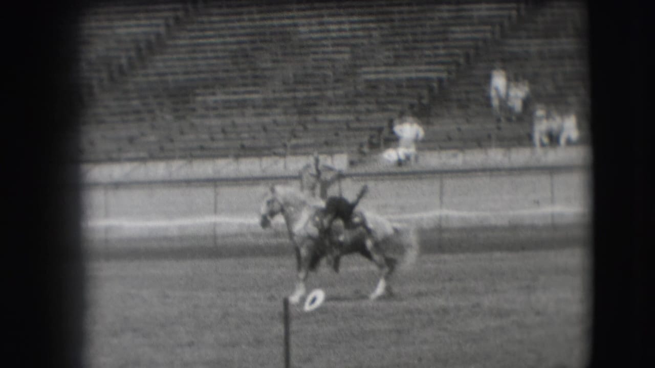 In 1941 Denver home-movie footage, a rider guides a horse across an open arena with sparse spectators in the bleachers.