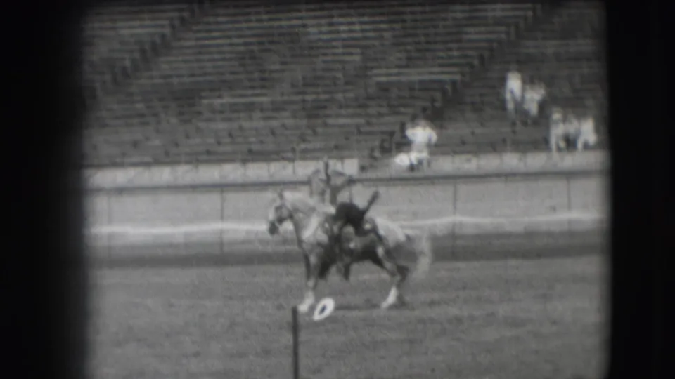 In 1941 Denver home-movie footage, a rider guides a horse across an open arena with sparse spectators in the bleachers.