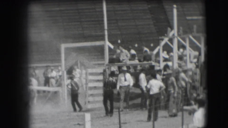 People cluster around the Denver rodeo chute area in 1941, with bleachers and arena structures behind them.