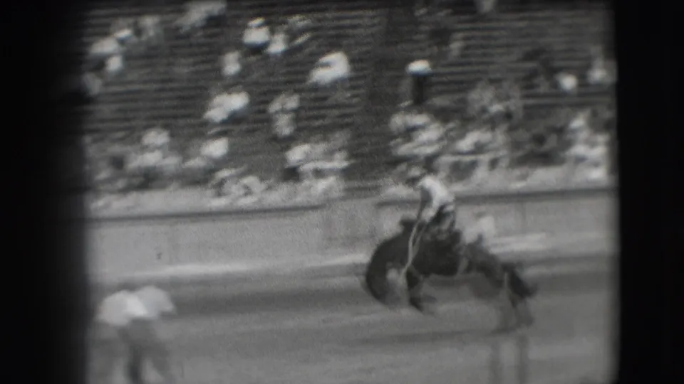 A rider in a light shirt attempts to stay on a bucking horse in a 1941 Denver rodeo arena.