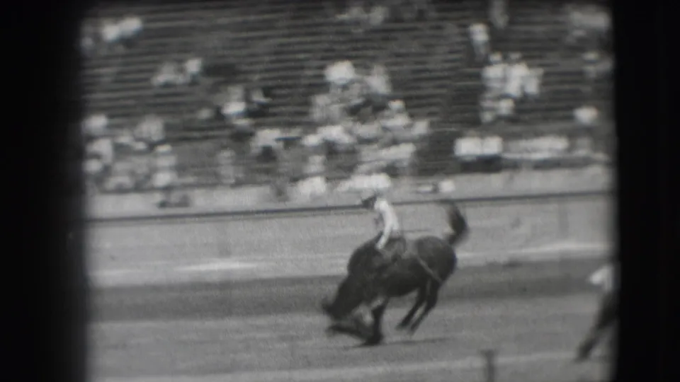 The bucking horse carries the rider across the Denver rodeo arena, with the 1941 crowd visible in the bleachers.