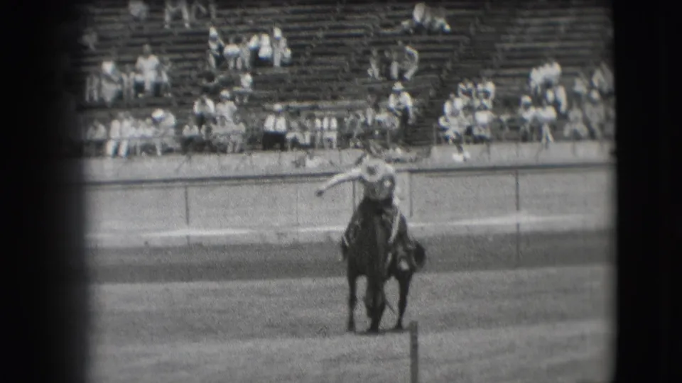 Cowboy appears to steady himself on a bucking horse during a 1941 Denver rodeo event, with bleachers behind.