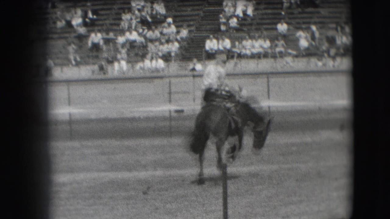 1941 Denver rodeo frame showing a cowboy on a dark horse in the dirt arena, with blurred bleachers and spectators in the background.