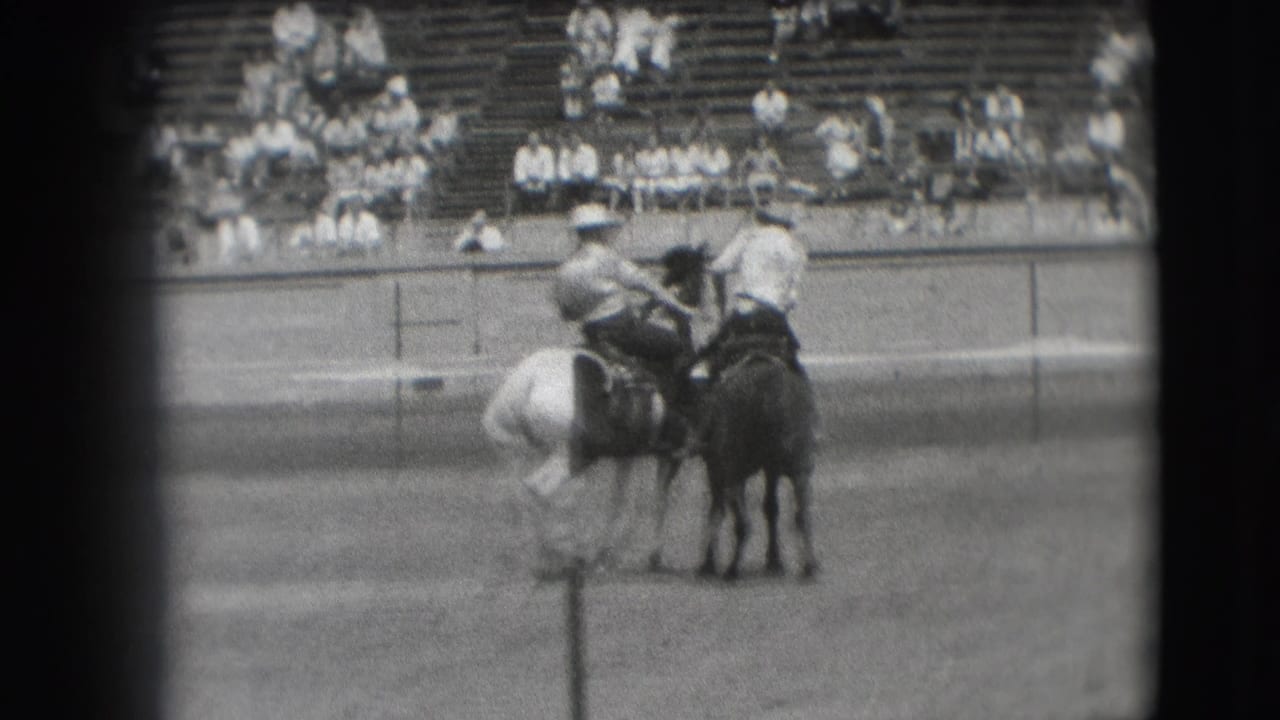 Two mounted cowboys pause or turn near each other in the rodeo arena.