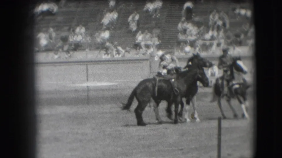 In 1941 Denver rodeo footage, several mounted cowboys appear near the arena rail while spectators watch from bleachers.