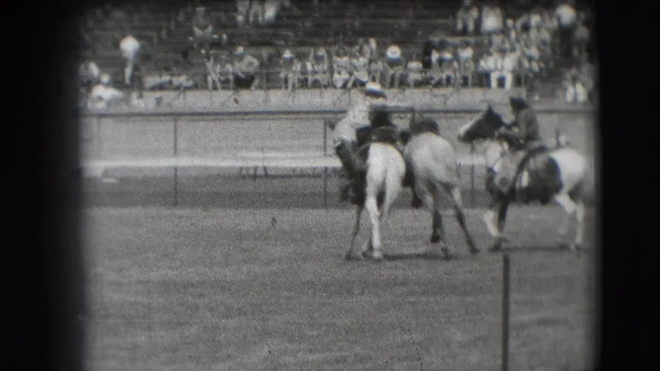 Cowboys on horseback appear near the arena rail in the stated Denver rodeo footage, with grandstand spectators in the background.