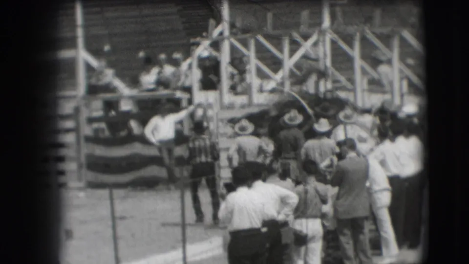 People gather near a decorated platform or judging area at the rodeo, with riders and spectators partly visible around it.