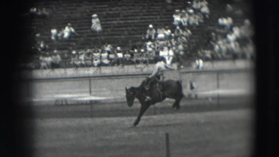 1941 Denver rodeo footage shows a cowboy in a light shirt on a bucking horse, viewed from the stands with arena rail and bleachers behind.