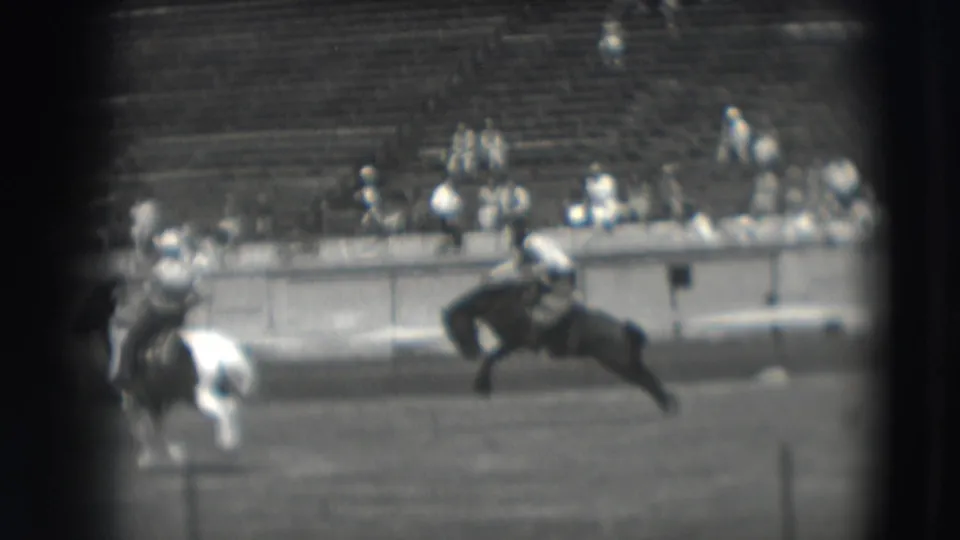 1941 Denver home-movie frame showing riders on horseback, including a pinto, moving across a stadium field before bleachers.