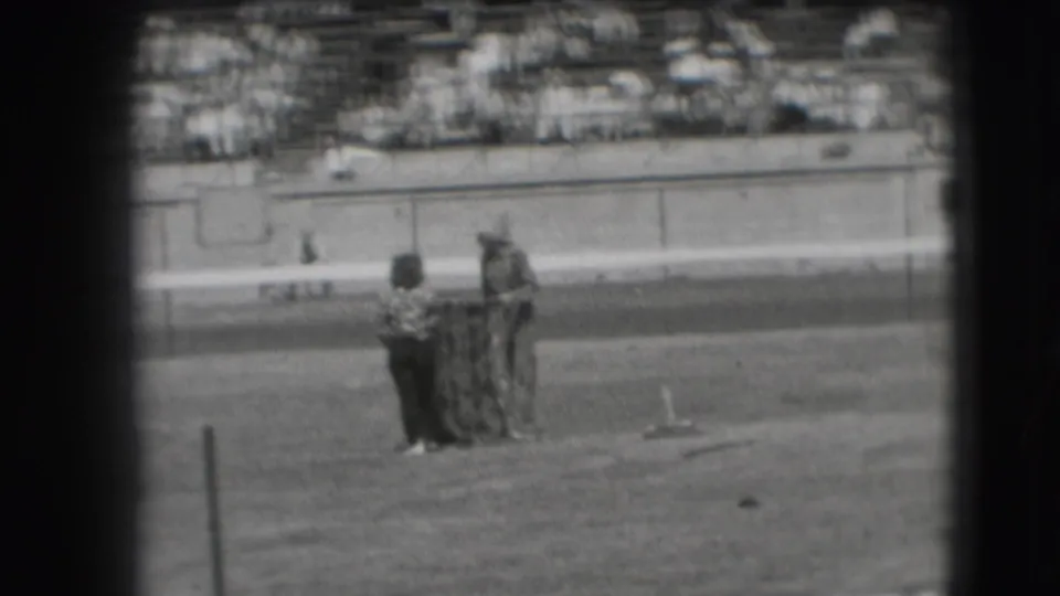 Several distant figures gather beside a horse in the 1941 Denver rodeo arena, with spectators seated behind them.