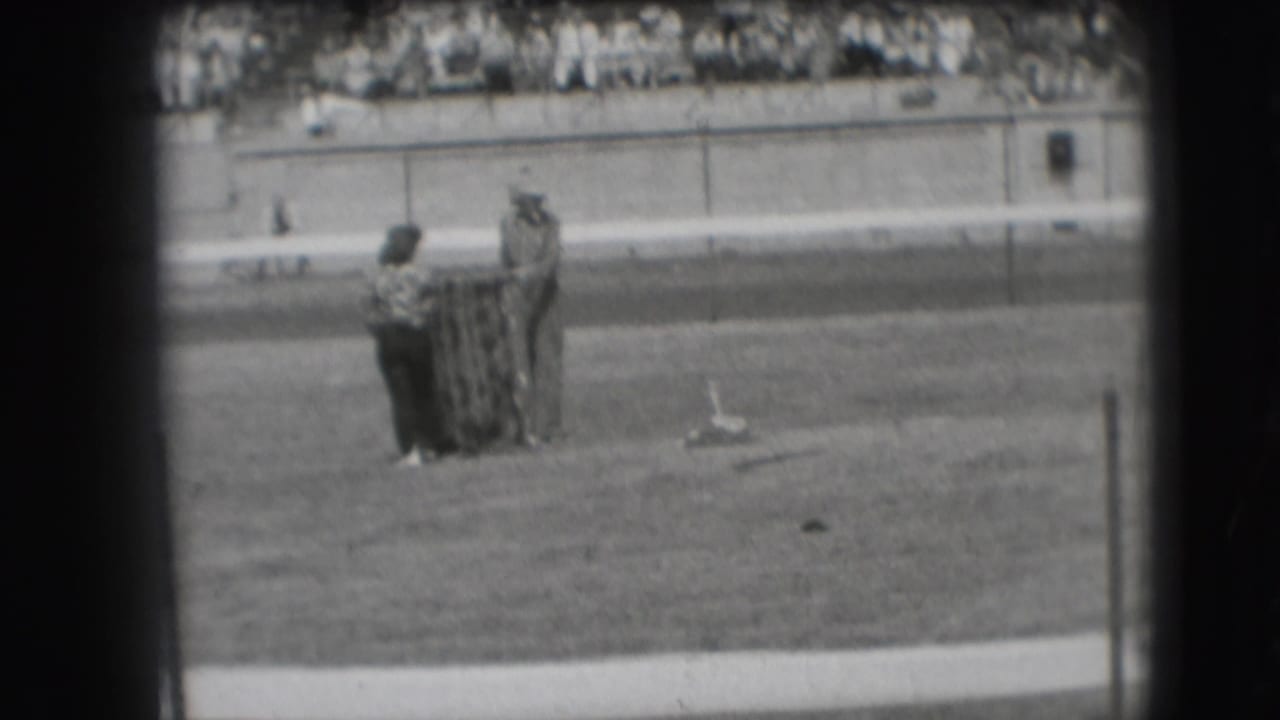 Two players remain beside the horseshoe pit with bleachers and seated spectators in the background.