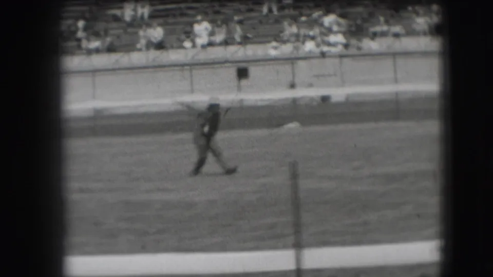 A man crosses the playing field near a horseshoe stake during the 1941 Denver recreation scene, with spectators visible in the bleachers.
