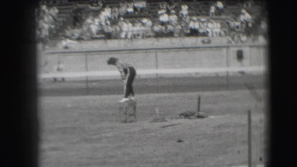 In 1941 Denver home-movie footage, a man stands on a small stool beside an open racetrack while spectators fill the background bleachers.