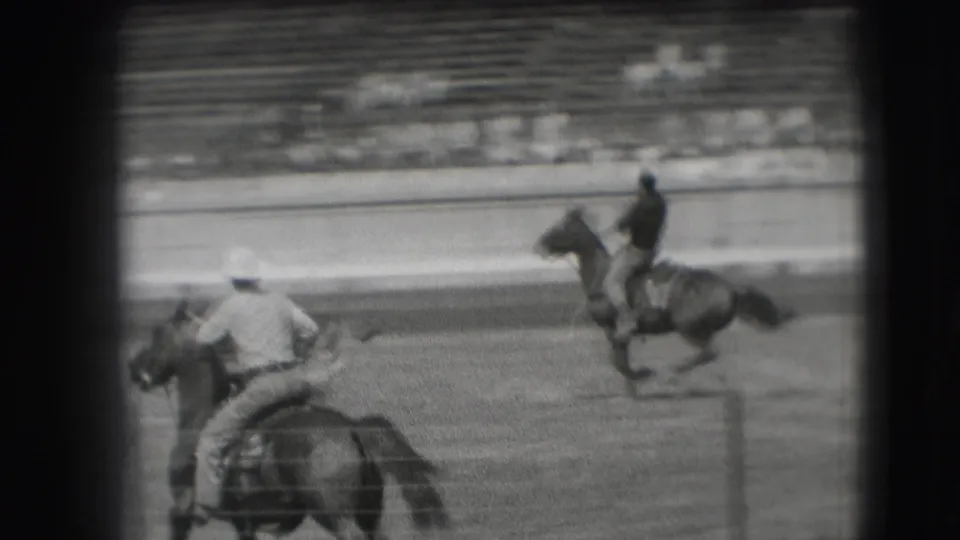 Two riders are visible on the 1941 Denver racetrack, one crossing the foreground and another moving along the far side before the stands.