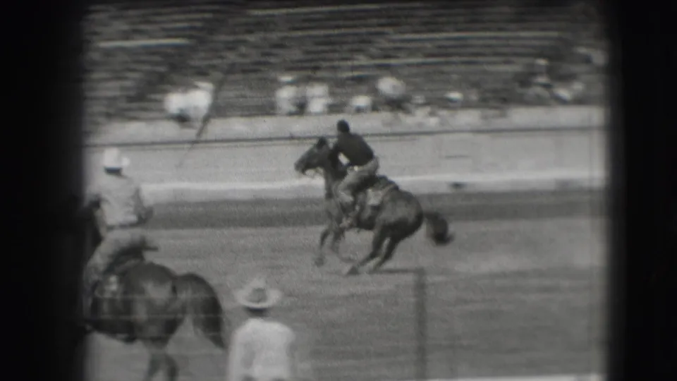 1941 Denver rodeo footage shows a mounted rider crossing the arena, with another horse and spectators visible near the stands.