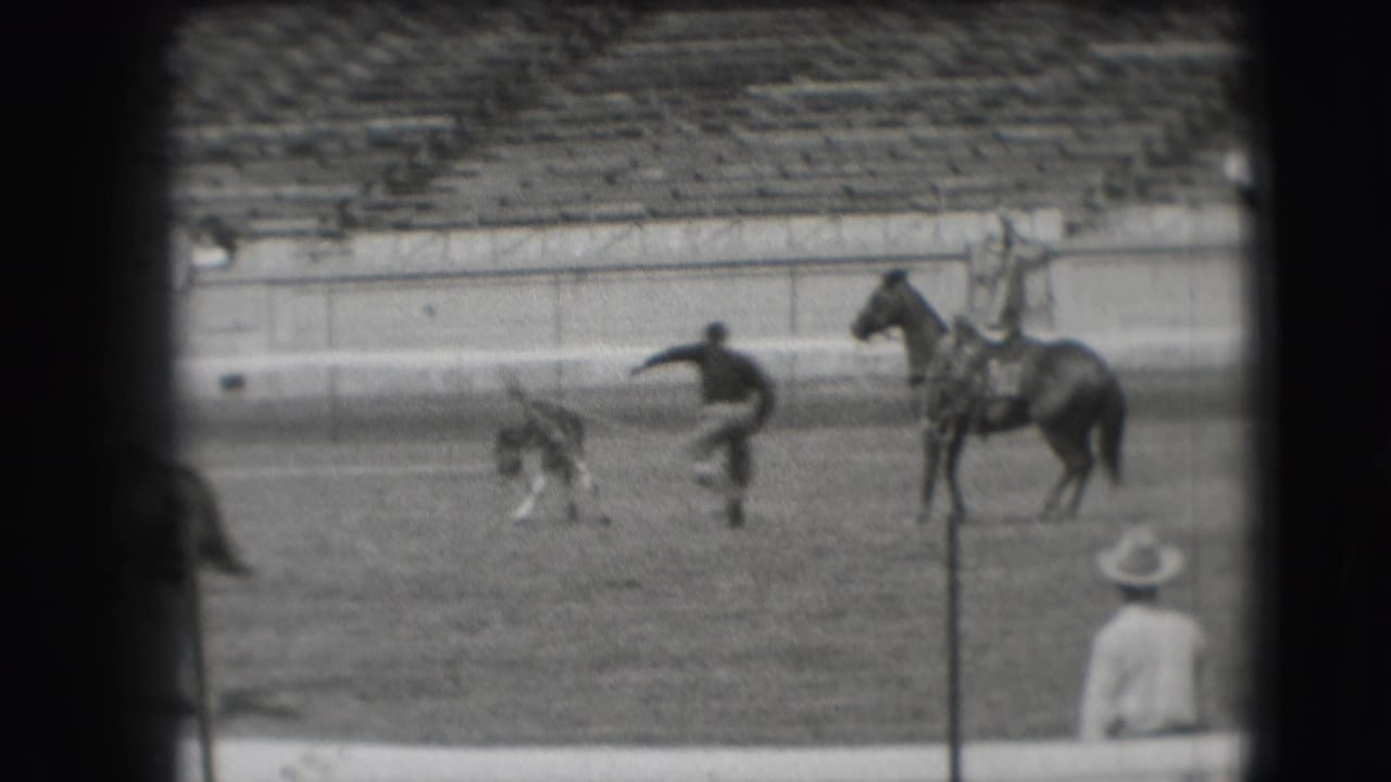 Cowboy runs or dismounts near a small animal while a horse stands nearby.