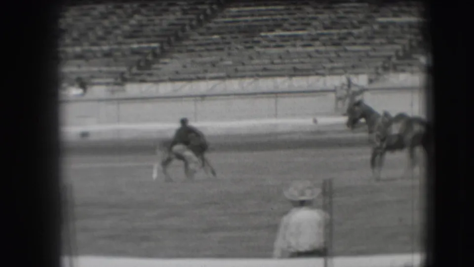 A cowboy in the 1941 Denver rodeo scene bends or crouches near a small animal, with a horse standing to the right.