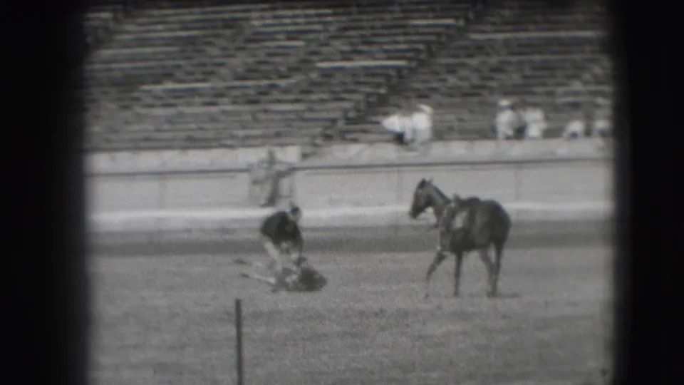 In supplied 1941 Denver rodeo footage, a man in dark clothing bends near a downed steer as a saddled horse stands nearby.
