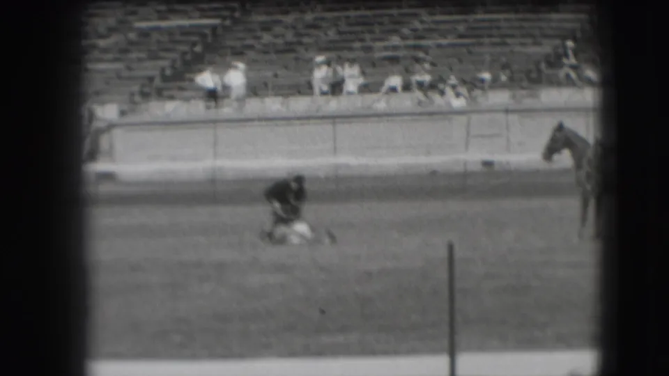 Final 1941 Denver rodeo frame shows the cowboy still over the roped animal, a horse at right, and scattered spectators in the bleachers.