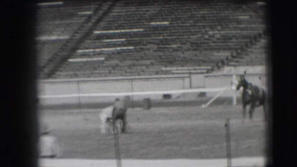 In 1941 Denver footage, a man on a grass sports field stands near a white horse while a mounted rider waits at the edge of the frame.