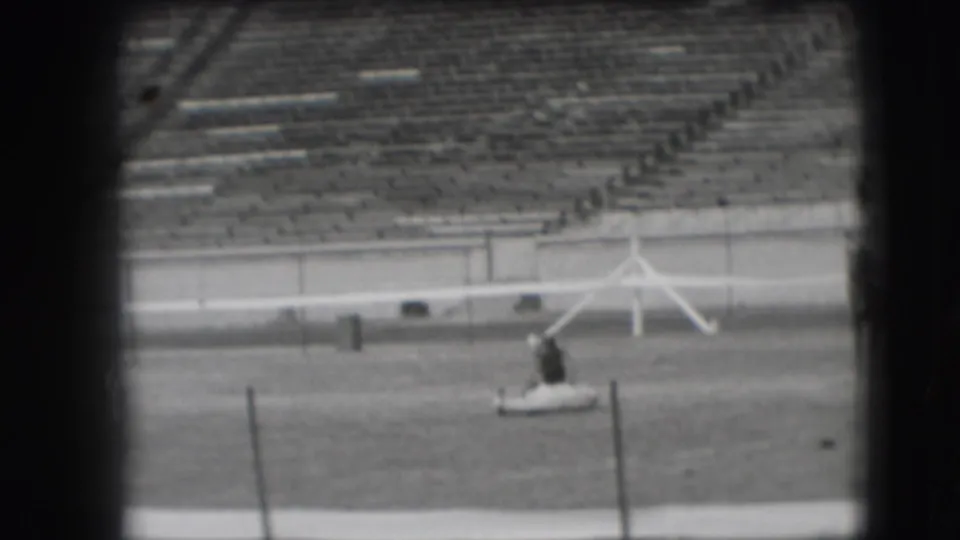 At the end of the clip, the handler stands near the white horse on the ground, with bleachers and field equipment in the background.