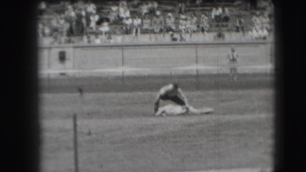 Cowboy bends over a steer in a rodeo arena with spectators in bleachers behind him.