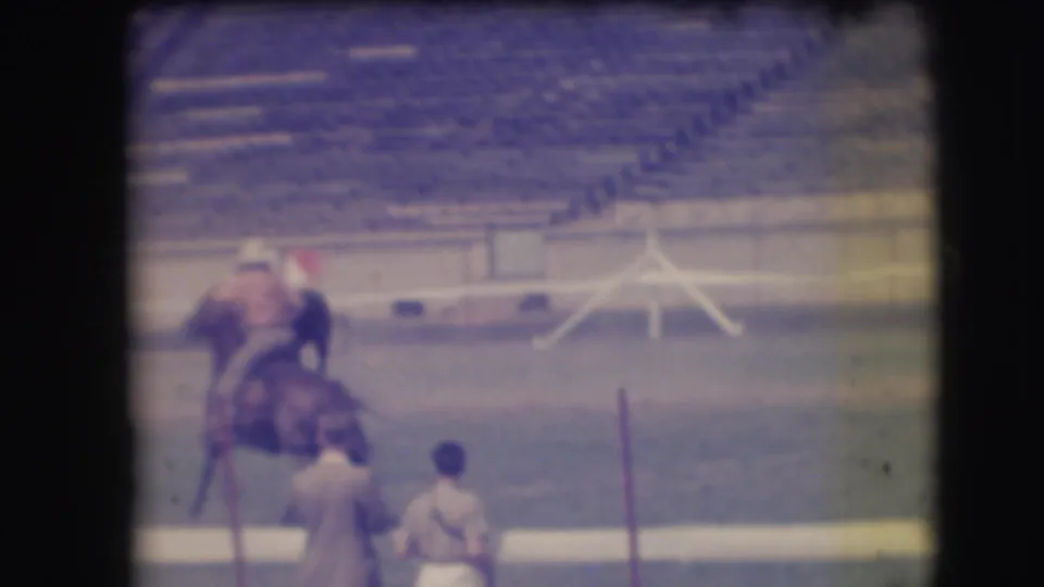 1941 Denver rodeo footage shows the rider close to a young horse while two bystanders stand near the arena edge.