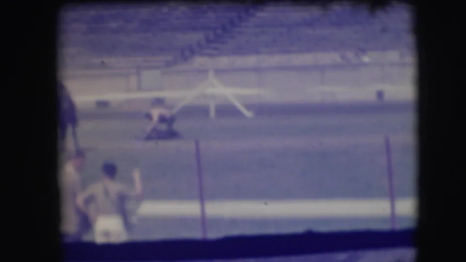 A Denver rodeo arena appears in soft 8mm color, with a cowboy near a cow and a spectator or participant partly visible in the foreground.