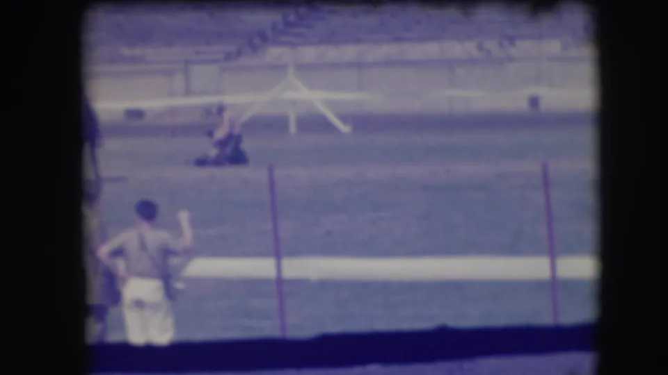 The 1941 Denver rodeo scene remains framed from the spectator area, showing a cowboy working near a cow with a foreground man partly in view.