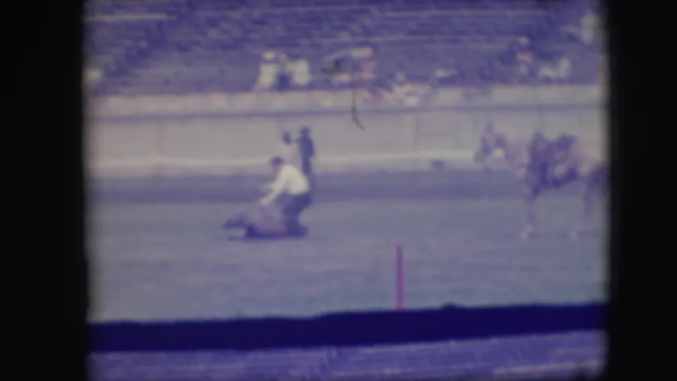 1941 Denver rodeo footage shows a mounted rider leaning toward a roped animal in a dirt arena with bleachers behind.