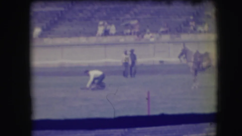 The home-movie frame shows a bent figure near the roped animal in a 1941 Denver rodeo arena with horses and spectators behind.