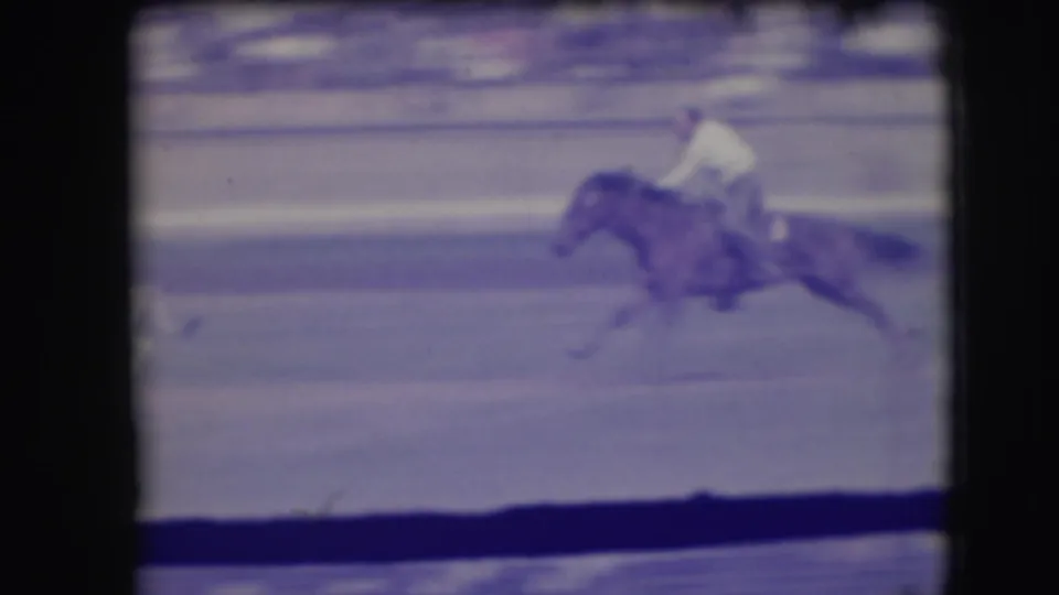 A mounted rider in a light shirt rides across the Denver rodeo arena, captured with motion blur and purple 8mm color shift.