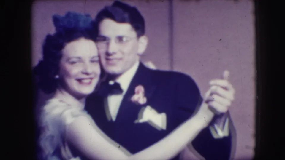 A woman with a hair accessory and a man in a tuxedo slow dance in the Joliet 1941 home-movie scene.