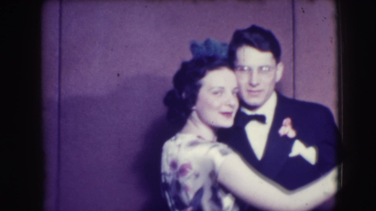 Couple in formal wear dancing close together against a purple wall.